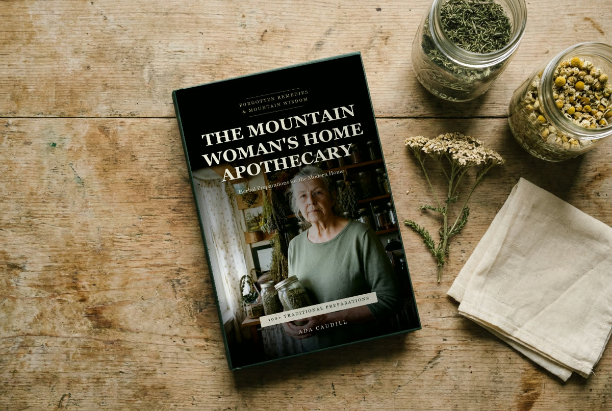 The Mountain Woman's Home Apothecary on a farmhouse table with jars of dried herbs